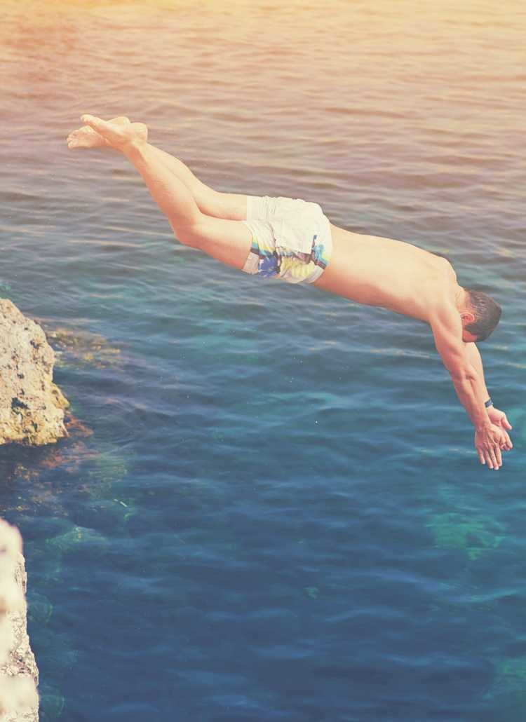 Man diving off cliff into ocean.